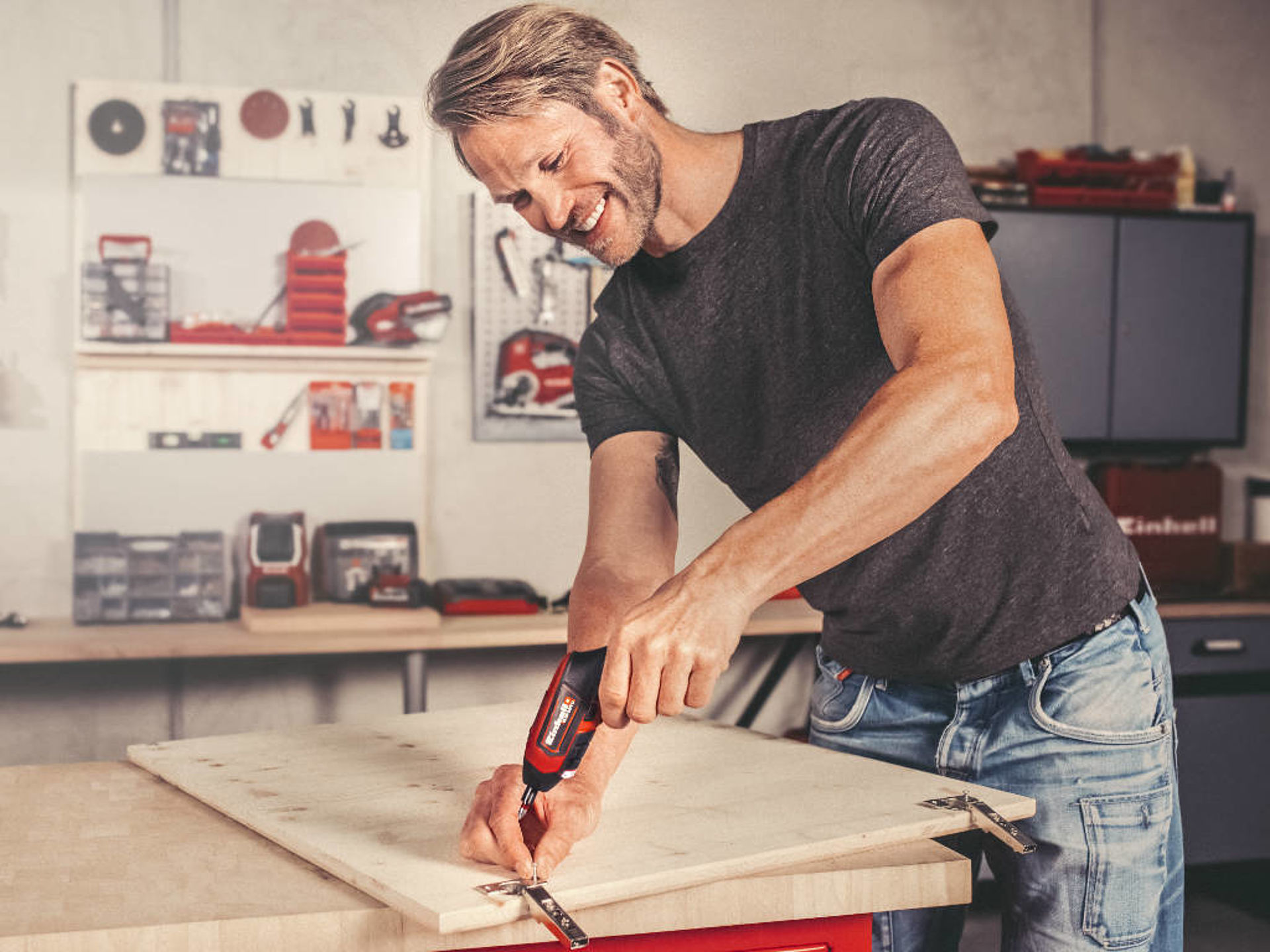 A man screws a hinge to a cabinet door with a cordless screwdriver. A man screws a hinge to a cabinet door with a cordless screwdriver.