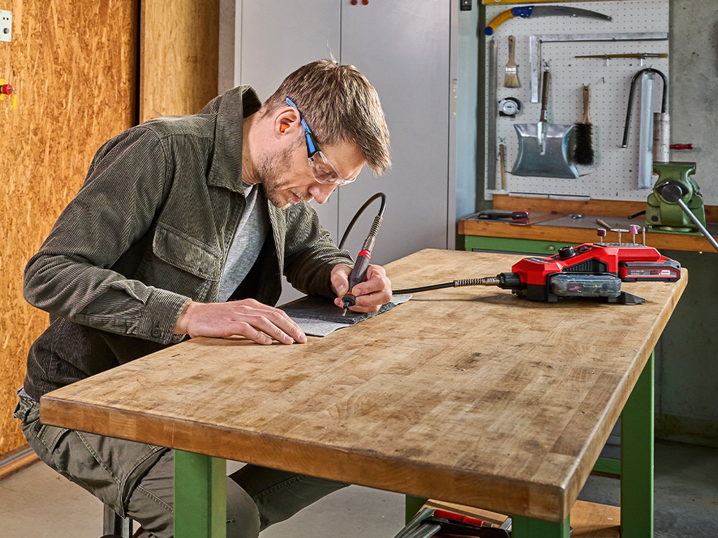 A man is working intently on a workpiece at a workbench using a cordless soldering iron.