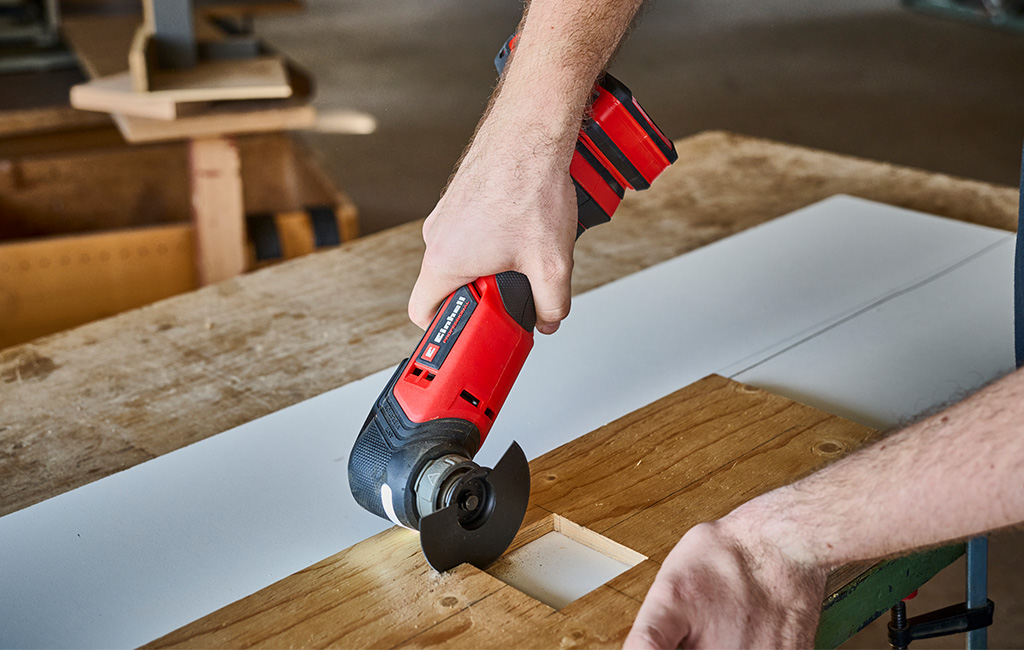 Detajlni posnetek rok, ki z Einhell akumulatorskim multitool orodjem izrezuje odprtino v leseno ploščo.