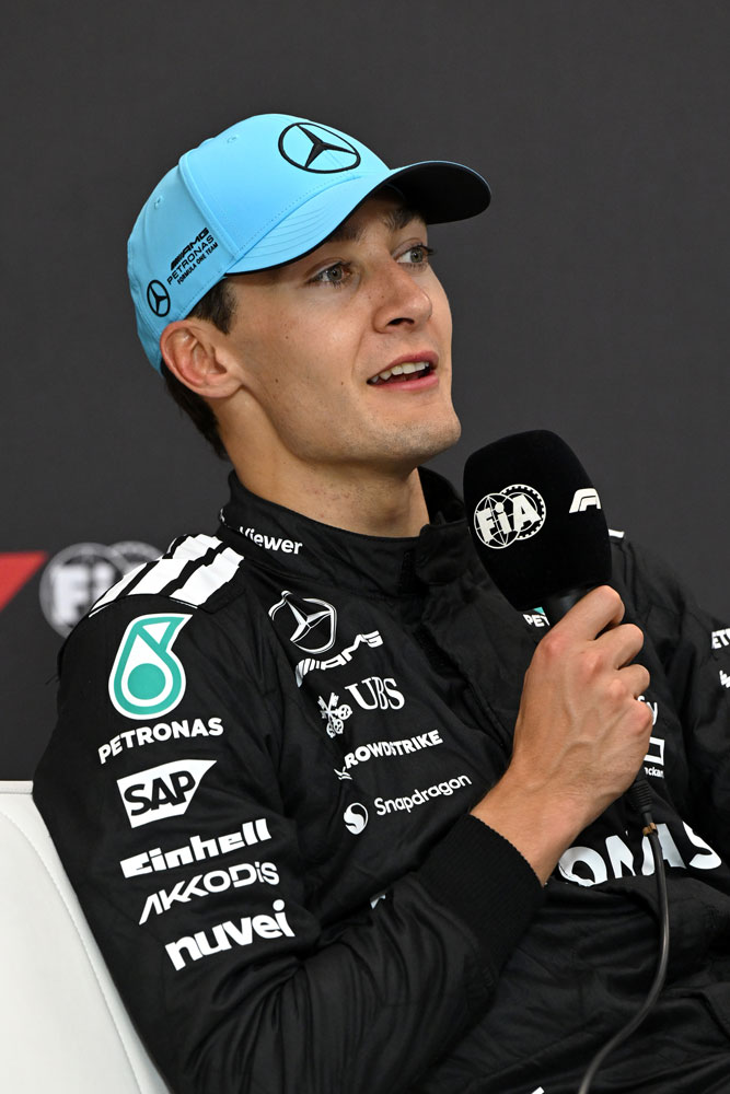 Dirkač Formule 1 George Russell z mikrofonom v desni roki.
