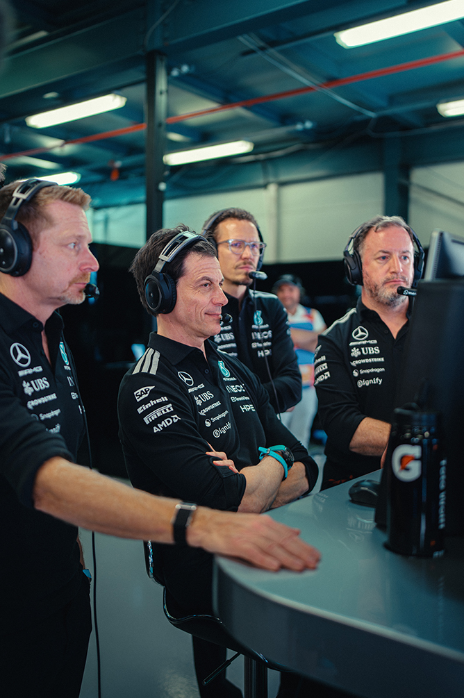 Člani ekipe Formule 1 s slušalkami spremljajo dirko iz pit zidu.