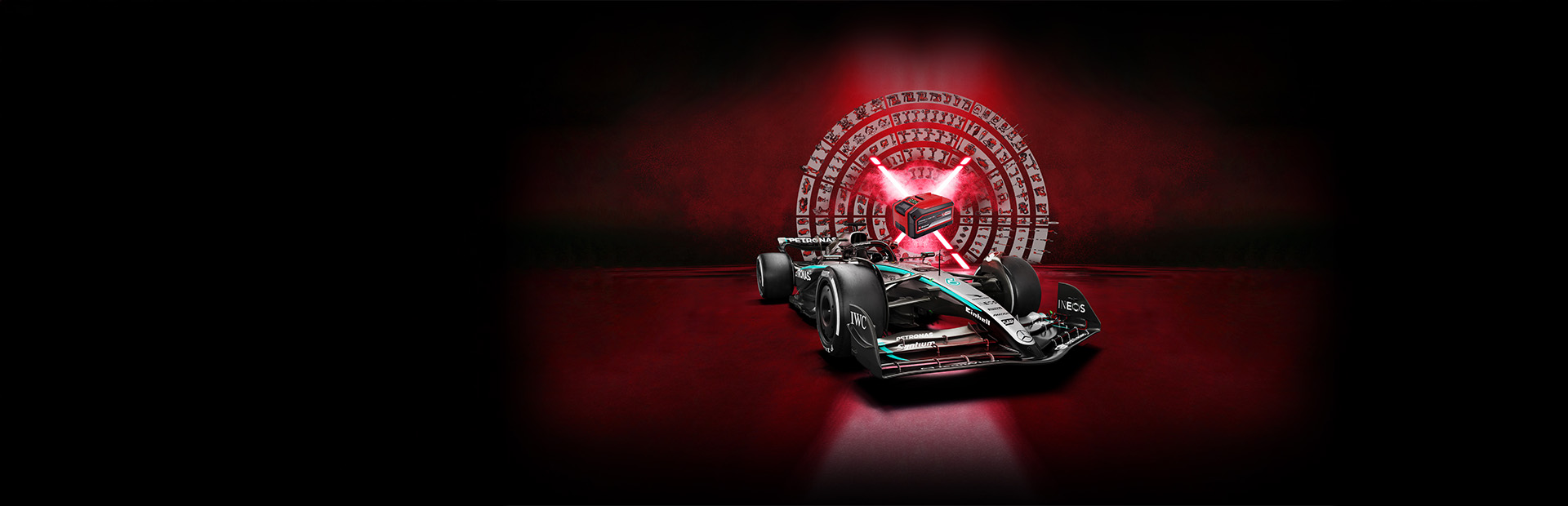 Ein Formel-1-Rennwagen von Mercedes-AMG PETRONAS steht vor einem roten Hintergrund mit einem zentralen Power X-Change Akku von Einhell, der von roten Lichtstrahlen angestrahlt wird.