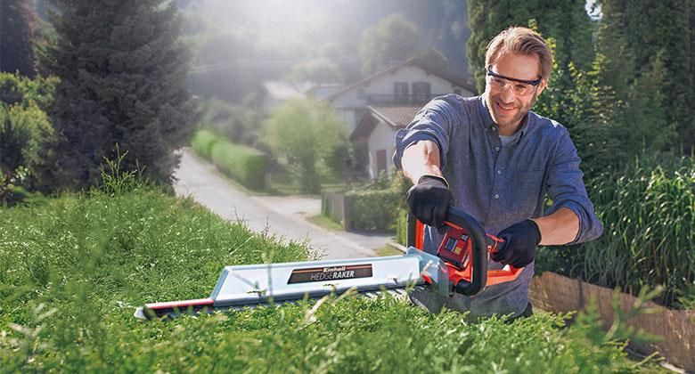 man cutting hedge with cordless hedge trimmer