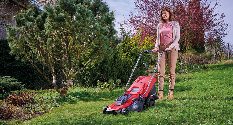 A woman mowing the lawn in a garden with a corded lawn mower.