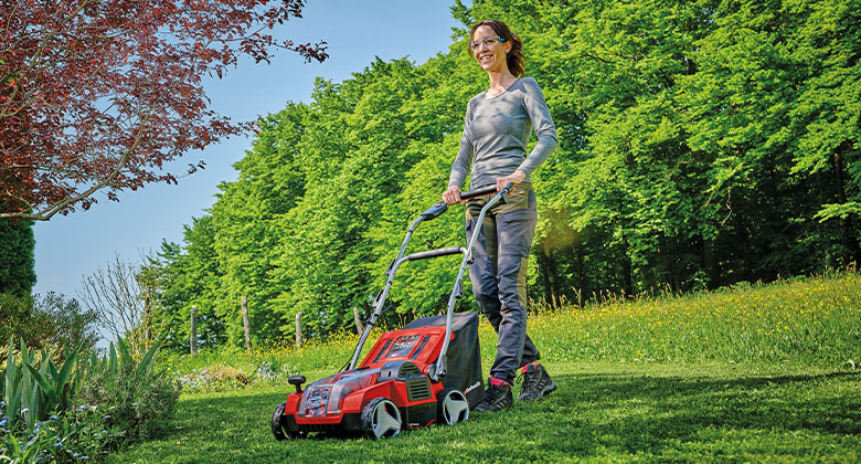 A woman scarifying a large lawn with a battery-powered scarifier.