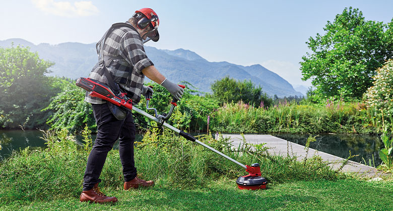 A man cuts tall grass with a battery-powered scythe from Einhell